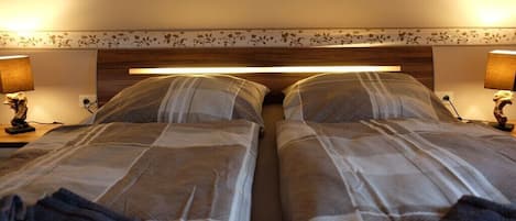 A hotel room with two beds, each with a headboard and bedside lamps.