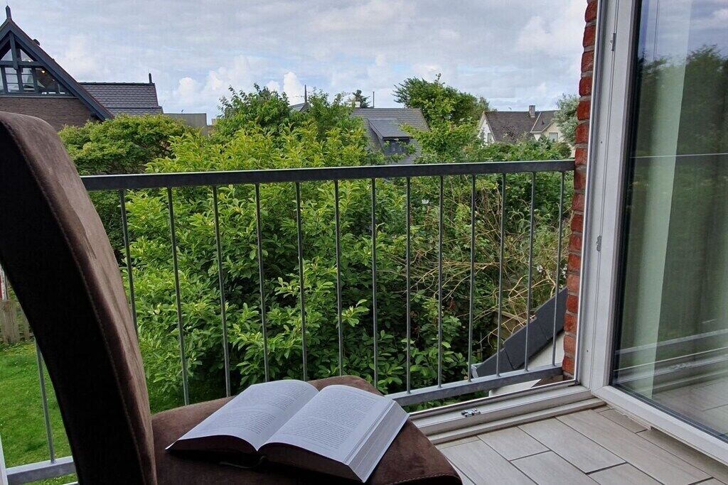 Ein Balkon mit einem Stuhl und einem offenen Buch, mit Blick auf einen Garten und angrenzende Häuser.