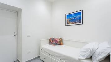 Ein Schlafzimmer mit einem Bett, einer weißen Tür, einem gerahmten Bild an der Wand und einer kleinen, weißen Kommode.