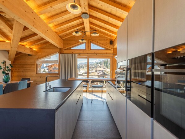 A modern kitchen with wooden beams, a large island, and a view of a mountainous landscape. - Modern apartment, jacuzzi - 14 guests (Les Gets)