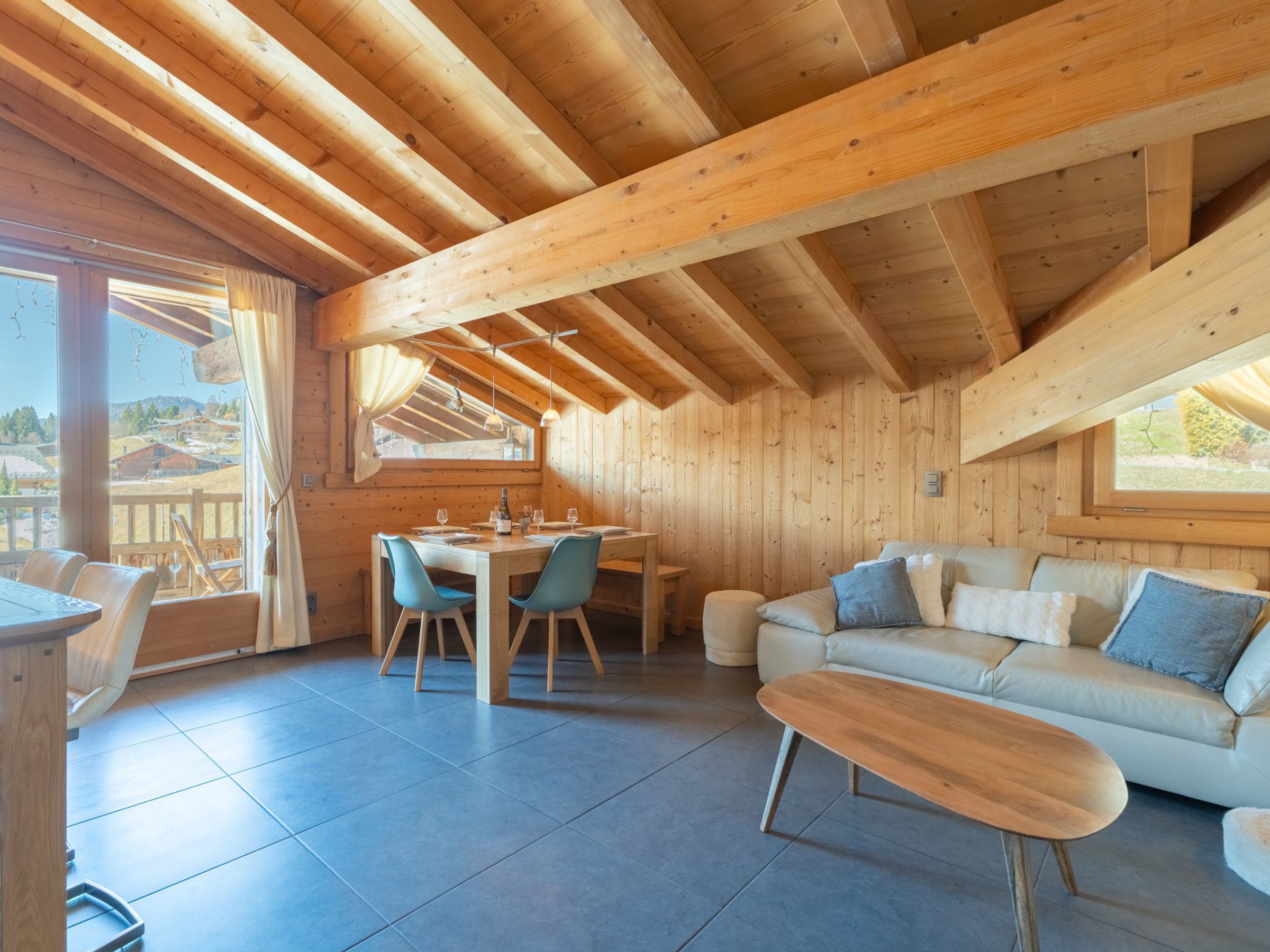 A wooden interior with a dining area, sofa, and large windows.