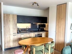 A compact kitchen with dark cabinets, a wooden dining table, and green upholstered chairs. - Spacious apartment with mountain view (Saint-Jean-d'Aulps)
