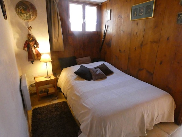 A bedroom with a bed, a nightstand, a lamp, a window, and wooden walls.