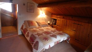 Une chambre mansardée chaleureuse, avec un lit, une table de chevet et une armoire en bois.