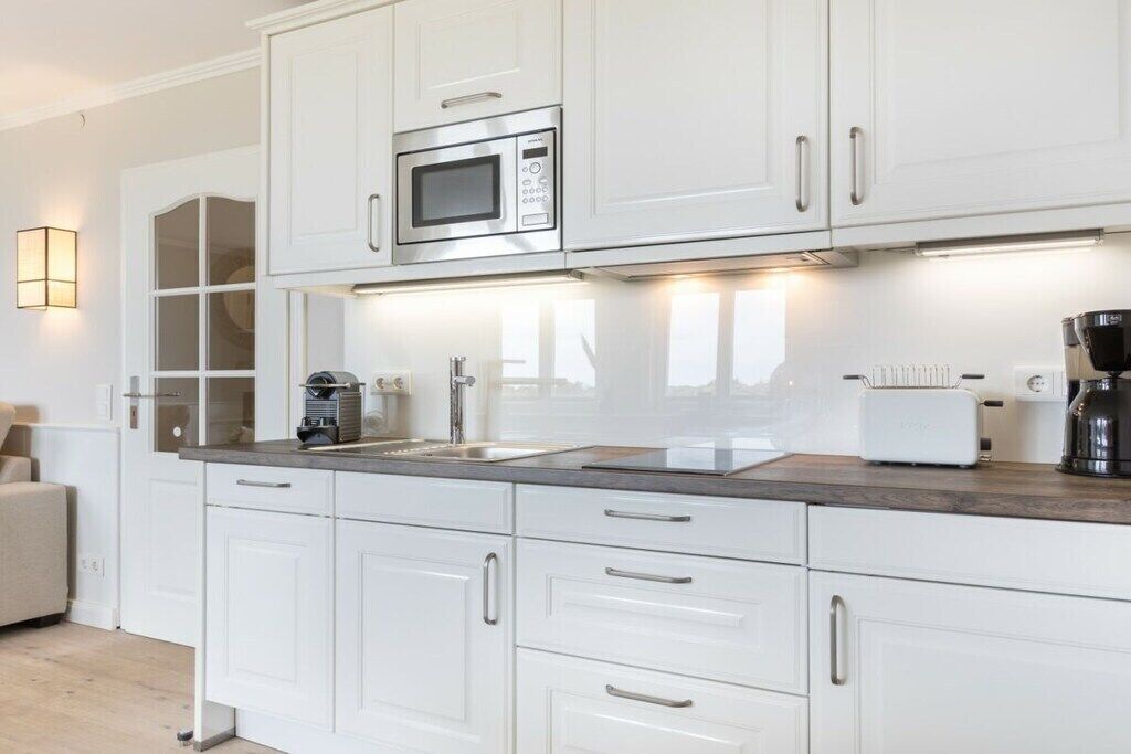 Una cocina moderna con gabinetes blancos, microondas integrado, cafetera y tostadora.