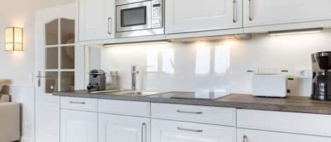 Una cocina moderna con gabinetes blancos, microondas integrado, cafetera y tostadora.