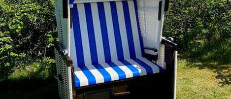 Una silla exterior azul y blanca a rayas con respaldo de malla, ubicada en una terraza de madera rodeada de vegetación.
