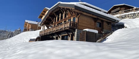 A wooden chalet with a balcony, set against a snowy landscape.