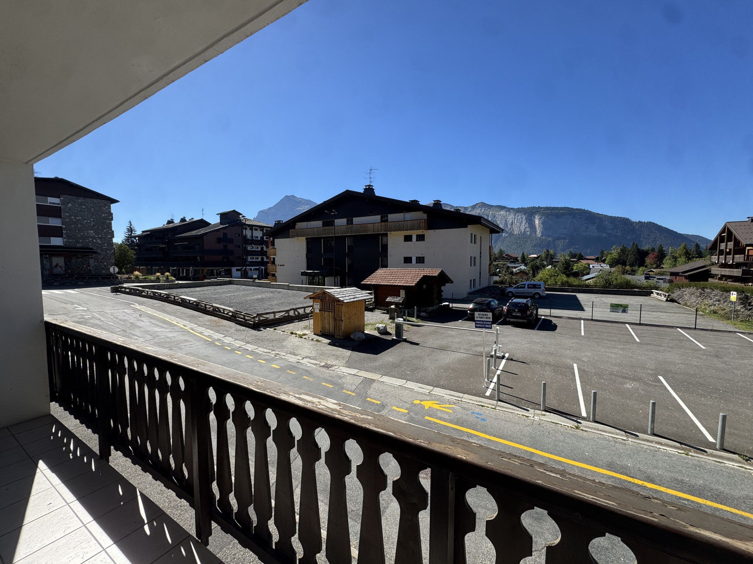 A balcony with a view of a parking area, buildings, and mountains.