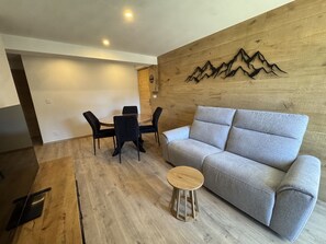 A modern living room with a grey sofa, a wooden coffee table, and a dining area with a round table and four chairs. - Renovated apartment - 4 guests (Les Carroz d'Arâches)