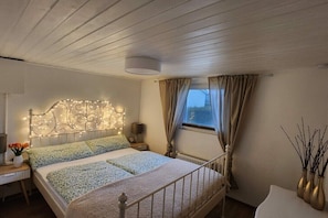 A bedroom with a bed, bedside tables, a nightstand, a window with curtains, and a wall-mounted light fixture. - Holiday home with 3 bedrooms (Wervershoof)