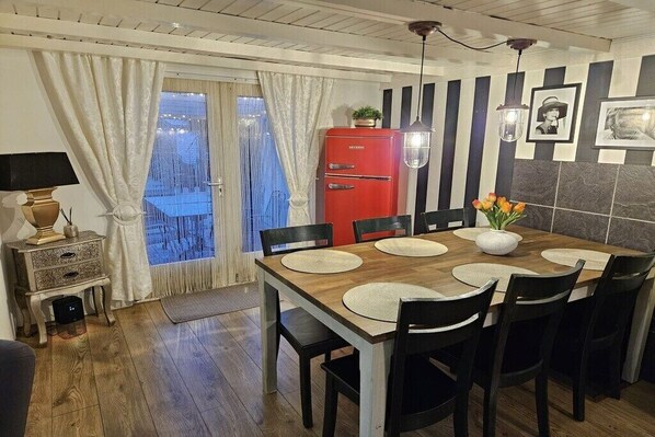 Een eetgedeelte met een houten tafel, zwarte stoelen en een rode koelkast.