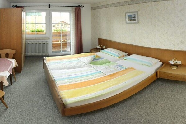 Quarto com cama, mesa de cabeceira, cadeira, mesa e janela com cortinas.