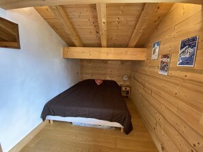 A bedroom with a wooden ceiling, a bed, a nightstand, and posters on the wall. - New chalet panoramic view - 8 guests (Arêches-Beaufort)