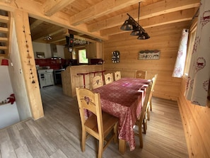 Un intérieur en bois comprenant une salle à manger avec une table dressée pour six personnes, un coin cuisine et un espace de vie.