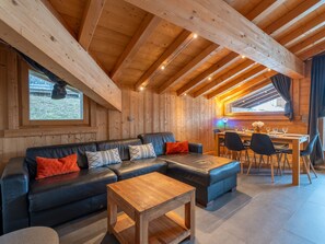 A cozy cabin interior with a wooden ceiling, a sofa set, a dining table with chairs, and a window overlooking a snowy landscape. - Ideal family apartment - 6 guests (Les Gets)
