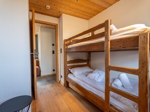 Ein Schlafraum mit Etagenbetten, Holzbalkendecke und einer Tür zu einem anderen Zimmer.