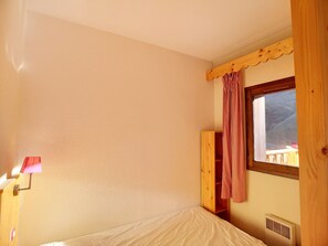 A small, single-bed room with a wooden headboard, a window with a view, and a bedside table with a lamp. - Cozy apartment with wifi - 6 guests, mountain view (Les Menuires)