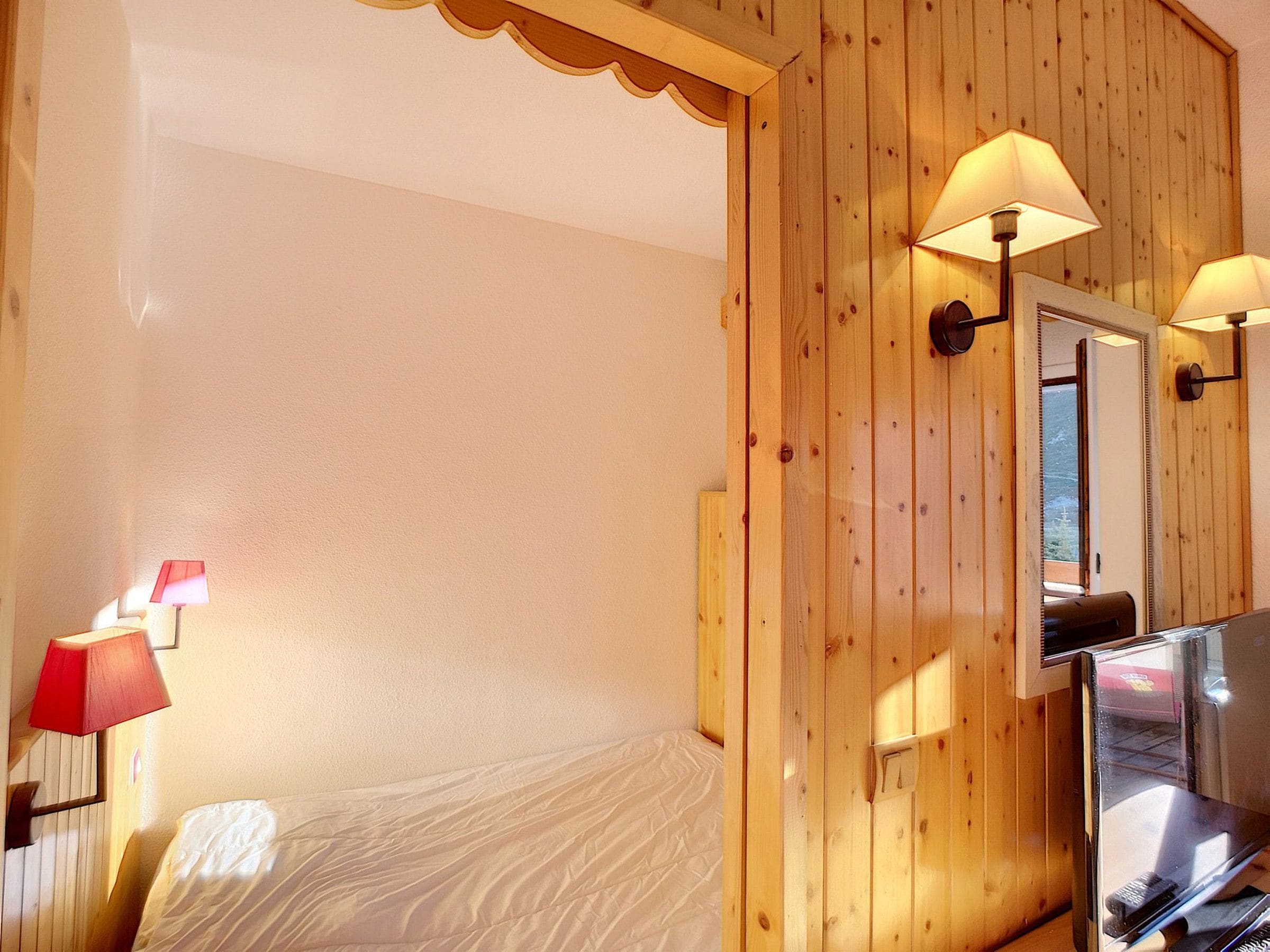 A hotel room with a bed, wooden panel walls, a mirror, and two wall-mounted lamps.