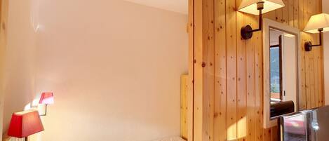 A hotel room with a bed, wooden panel walls, a mirror, and two wall-mounted lamps.