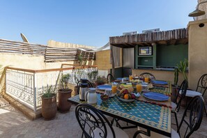 An outdoor dining area with a table set for breakfast, surrounded by potted plants and a thatched roof structure. - Vrbo Property (Marrakesh)