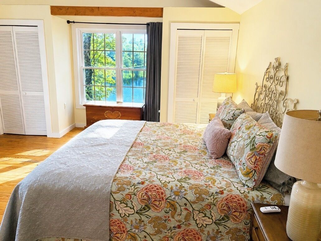 Een slaapkamer met een groot bed, een nachtkastje, een lamp en een raam met gordijnen.