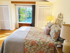 Un dormitorio con una cama grande, una mesita de noche, una lámpara y una ventana con cortinas.