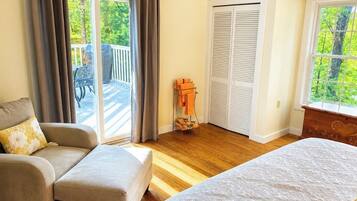 A bedroom with a bed, a sofa, a sliding glass door to a balcony, and a closet with white shutters.