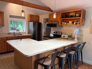 A kitchen with a large island, wooden cabinets, stainless steel appliances, and bar stools.