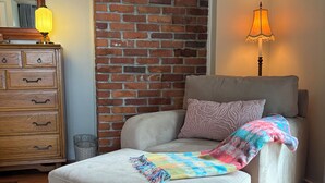 Un dormitorio con cama, cómoda, lámpara y pared de ladrillo.