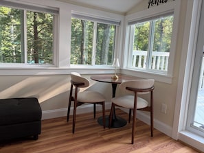 A room with a dining table and chairs, large windows with a view of trees, and a dark-colored sofa.