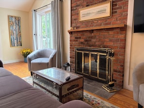 A living room with a fireplace, a sofa, a chair, and a vintage trunk.