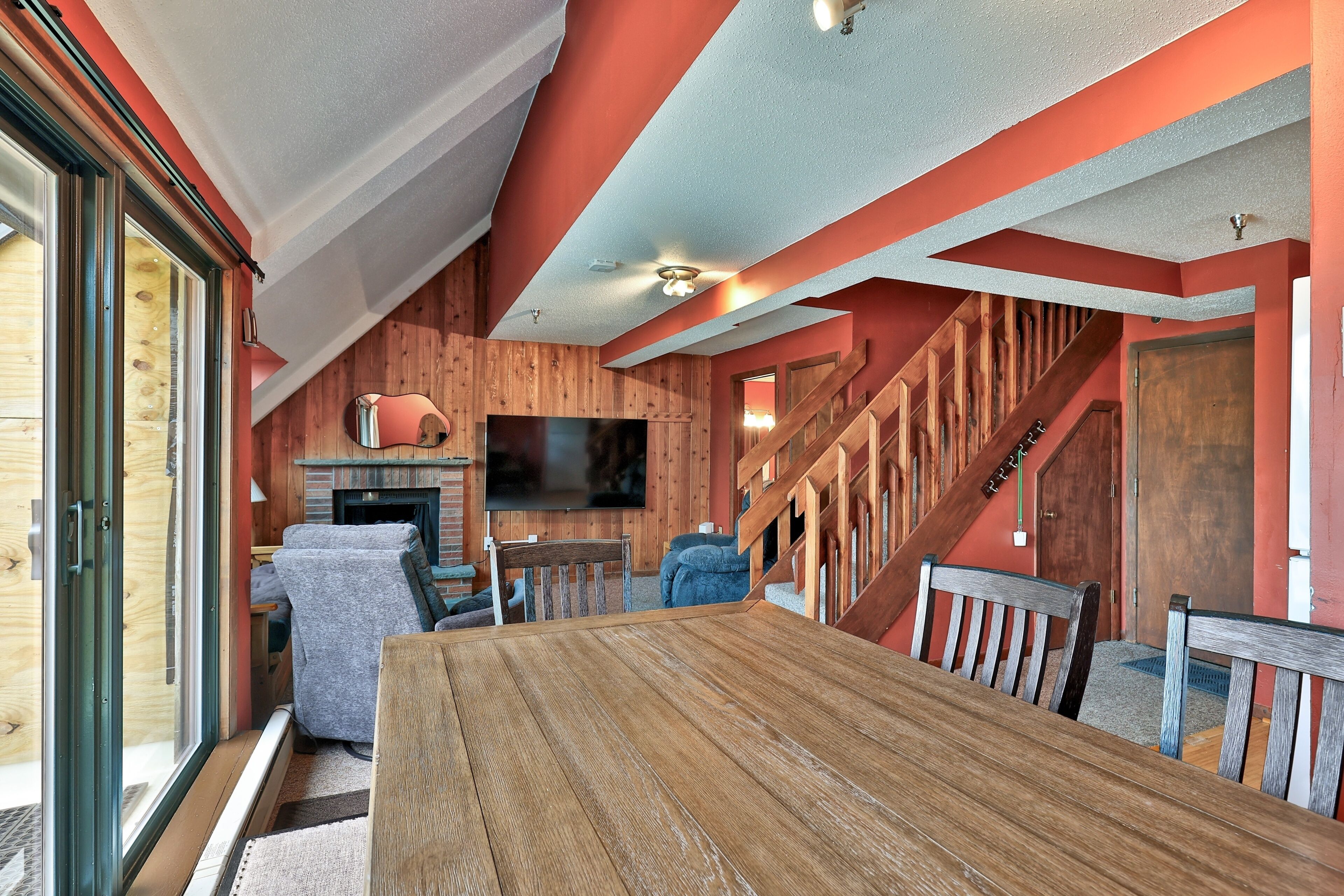 Ein gemütliches Interieur mit einem Holzesstisch, einem an der Wand befestigten Fernseher und einer Treppe, die zu einer anderen Ebene führt.