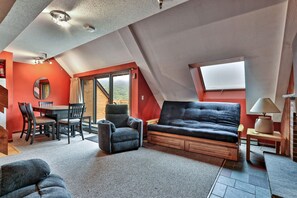 A cozy loft bedroom with a sloped ceiling, a sofa bed, a dining table with chairs, and a large window offering a view. - Mountain Green Condo 3f11 2 Bedroom Condo (Killington)