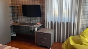 Et moderne værelse med et vægmonteret fladskærms-tv, et lille skrivebord med vask, en grå opbevaringsenhed og en gul beanbag-stol.