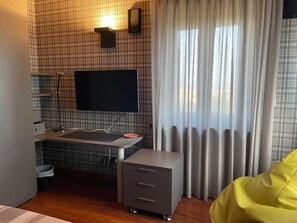 Habitació moderna amb televisió de pantalla plana penjada a la paret, un petit escriptori amb un rentanet, un moble d'emmagatzematge gris i un seient informal de color groc.