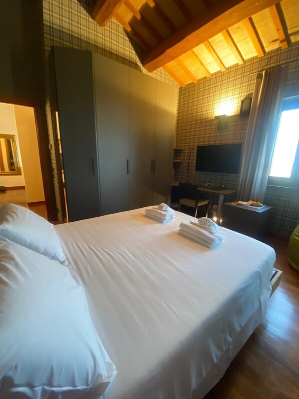 Habitació d'hotel amb un llit gran, un armari, una taula de nit amb cadira i una televisió.