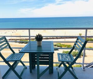 Een balkon met een tafel en twee stoelen, met uitzicht op een strand.