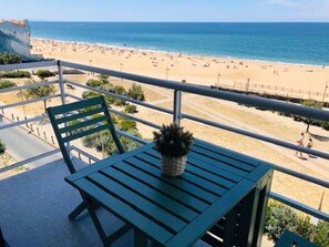 A balcony with a green table and chair, overlooking a beach with people and a clear sky. - Exceptional Ocean View in Hossegor. (Soorts-Hossegor)