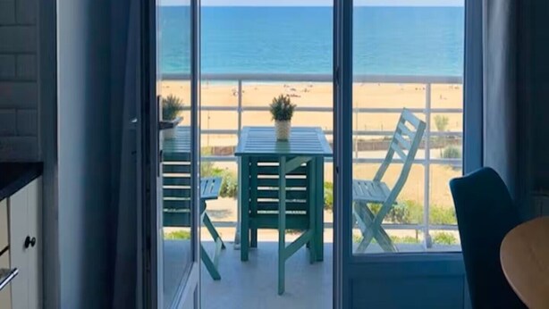 Uma varanda com vista para a praia, uma mesa e duas cadeiras.