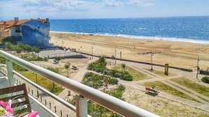 Uma praia com um edifício ao fundo, céu claro e vista para o oceano.