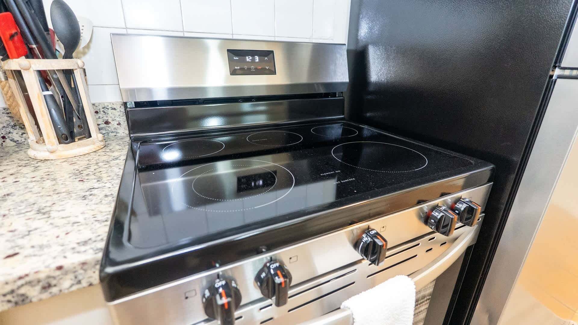 Une cuisinière en acier inoxydable, dotée de quatre brûleurs et d’un écran numérique, située dans une cuisine avec un comptoir en granit.