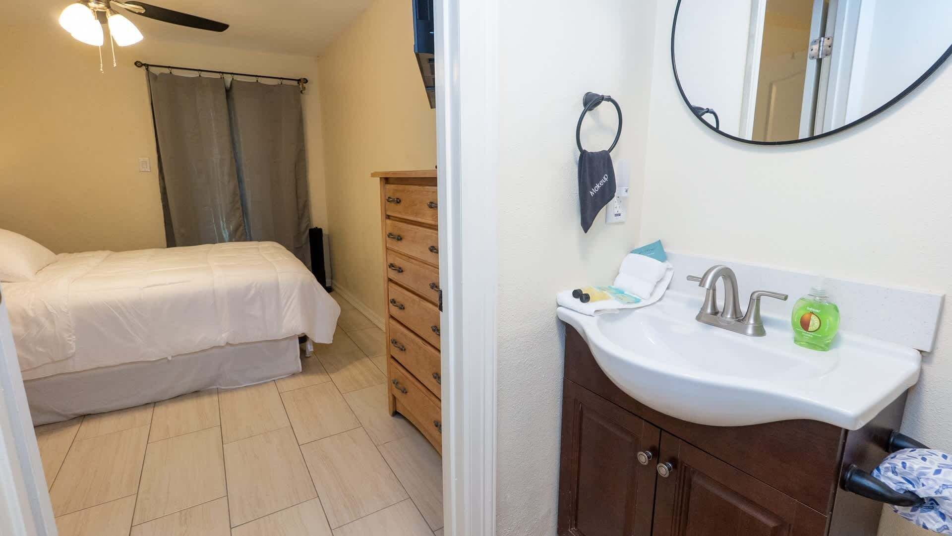 A bedroom with a bed, a dresser, a bathroom with a sink and mirror, and a ceiling fan.