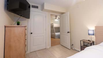 Une chambre à coucher avec un lit, un téléviseur fixé au mur, une table de chevet avec une lampe et une porte donnant accès à une salle de bain avec un lit superposé.
