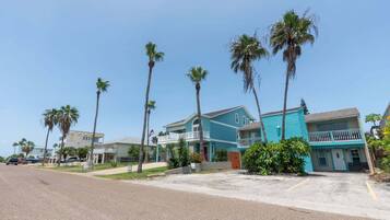 A coastal street lined with palm trees and two-story buildings with balconies.