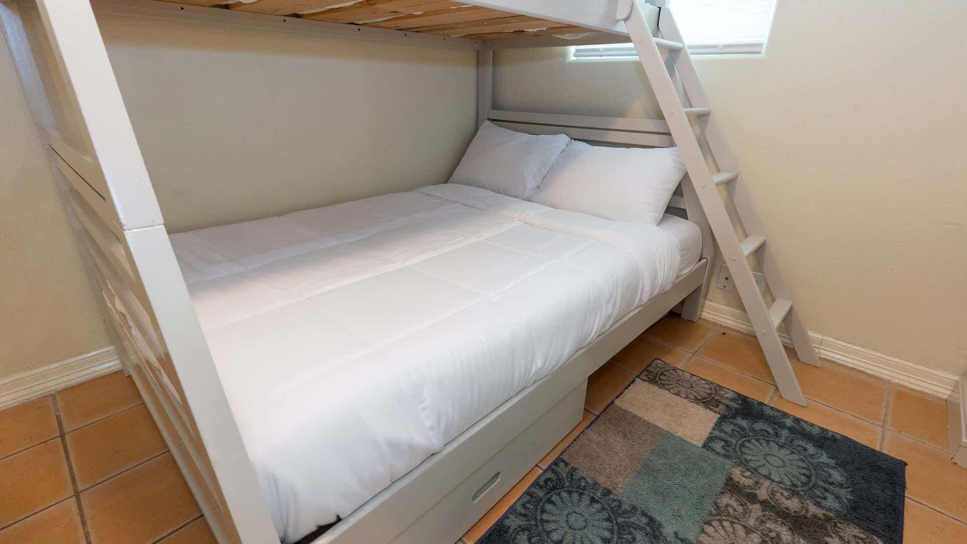 A bunk bed with a ladder, white bedding, and a patterned rug.