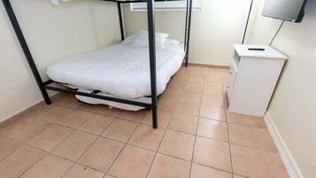 A single bed with a metal frame and white bedding in a room with tiled flooring and a small white cabinet.