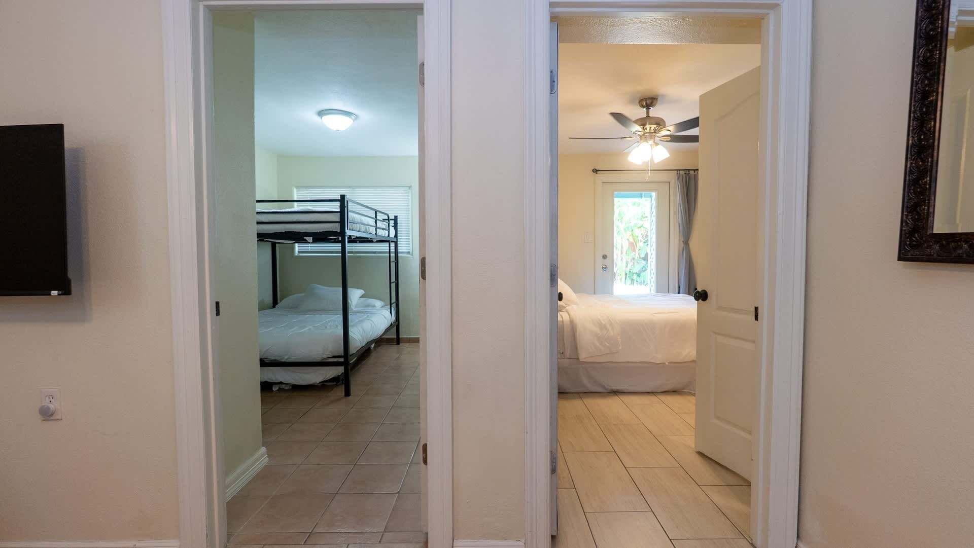 Un couloir avec un lit superposé et un lit simple, un ventilateur de plafond et une porte donnant sur une autre pièce.