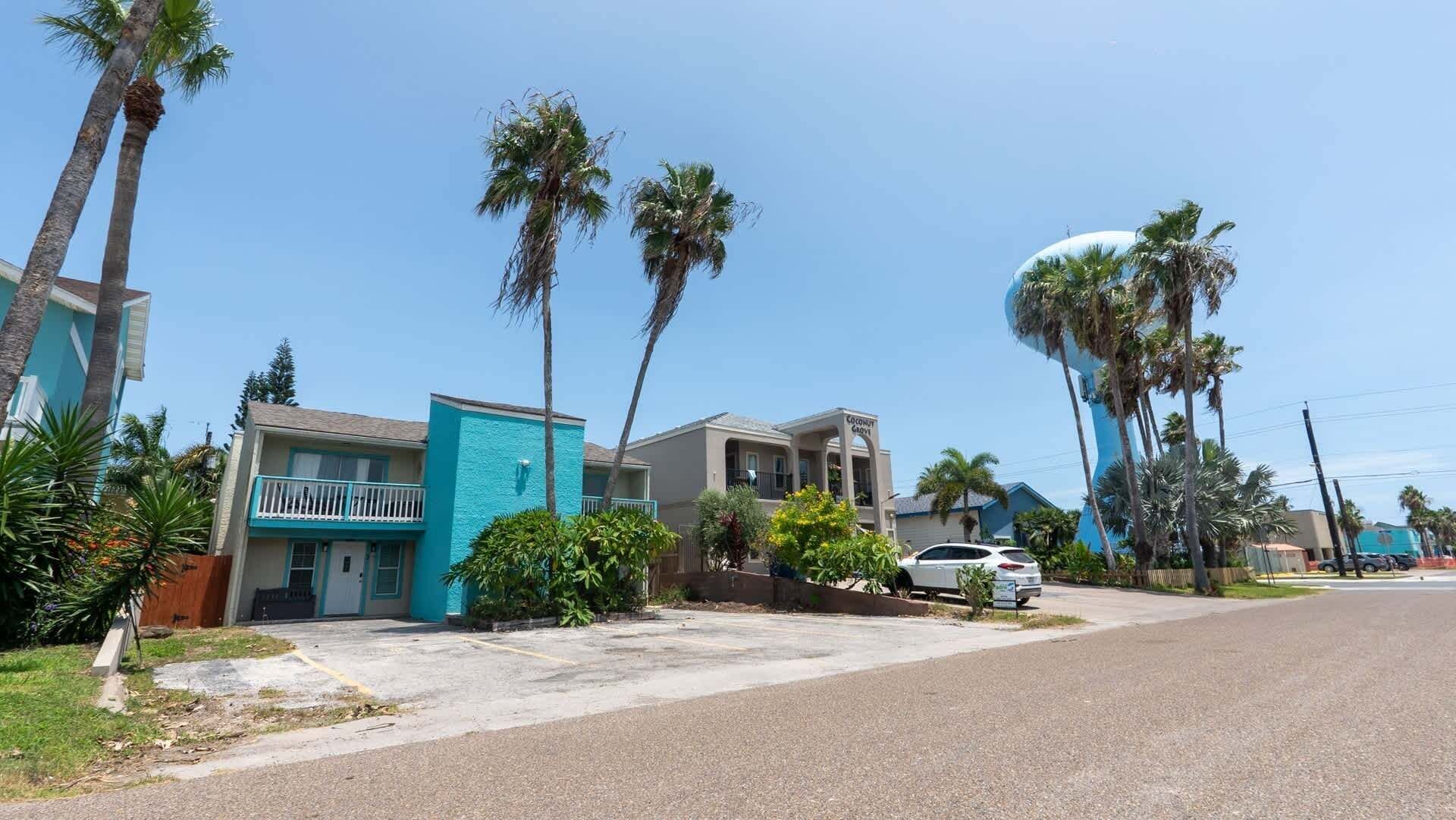 A residential street with houses, palm trees, and a parked car.