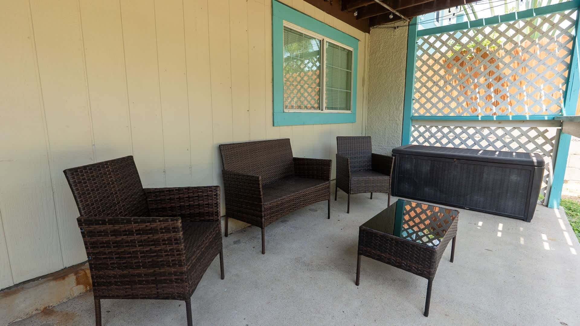 Un área de estar al aire libre con mobiliario de mimbre, incluyendo un sofá, dos sillones y una mesa de centro.